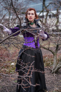 Portrait of Valerie as Lady Delilah Briarwood, peering through the branches of a leafless tree.